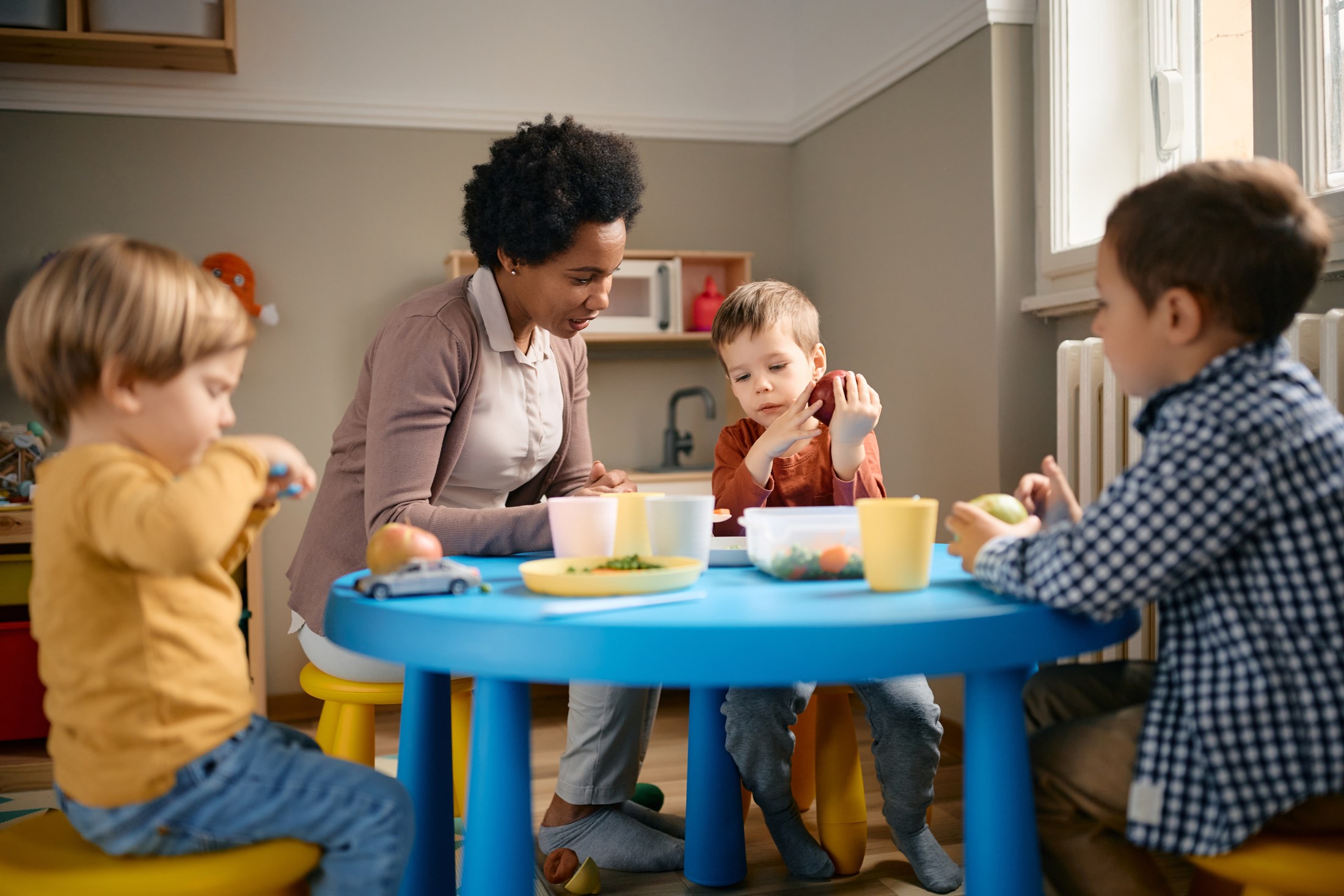 Early years practitioner sitting with toddlers at a low table at lunchtime