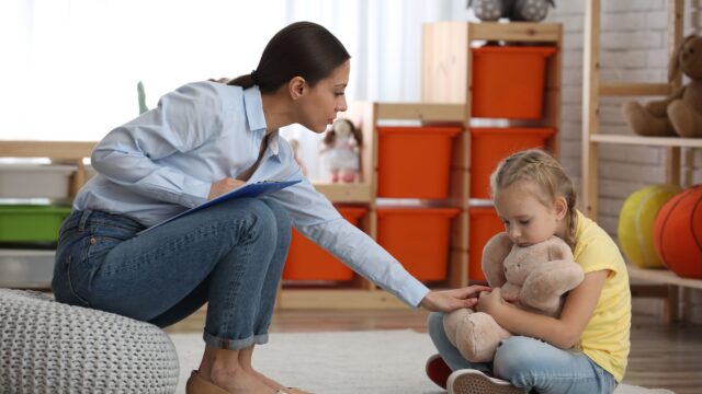 Practitioner kneeling to comfort a child holding a toy bunny